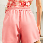 Back view of a woman wearing a floral top and pink shorts with an elastic waistband