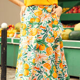 Woman wearing a printed skirt with an orange pattern in front of a fruit stand.