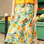 Person wearing a yellow top and a colorful wrap skirt with citrus fruit pattern outdoors.