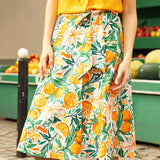 Person wearing a yellow top and a colorful wrap skirt with citrus fruit pattern outdoors.