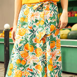 Woman wearing a skirt with a bow and a colorful fruit pattern in an outdoor setting.