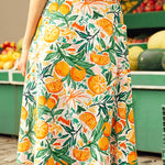 Woman wearing a skirt with a colorful fruit pattern in front of a fruit stand.