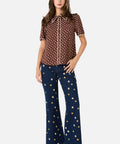 Woman wearing a brown daisy polka dot blouse and blue jeans with white floral polka dots on a white background