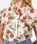 Person wearing a floral blouse with red apples and green leaves on a white background