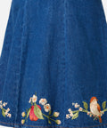 Blue denim skirt with floral and bird embroidery on a white background