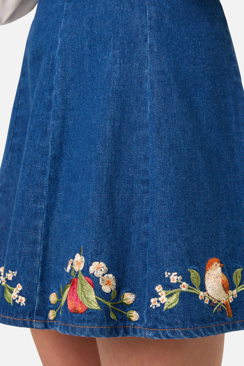Blue denim skirt with floral and bird embroidery on a white background