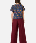 Woman wearing a patterned top and burgundy pants on a white background
