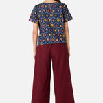 Woman wearing a patterned top and burgundy pants on a white background