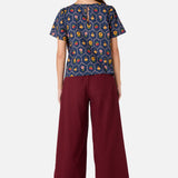 Woman wearing a patterned top and burgundy pants on a white background