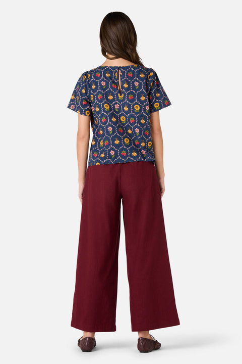 Woman wearing a patterned top and burgundy pants on a white background