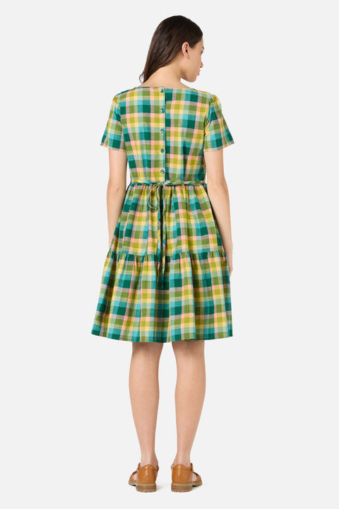 Back view of woman wearing a green and yellow checkered dress on a white background