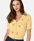 Woman wearing a yellow cardigan with floral and bee embroidery on a white background