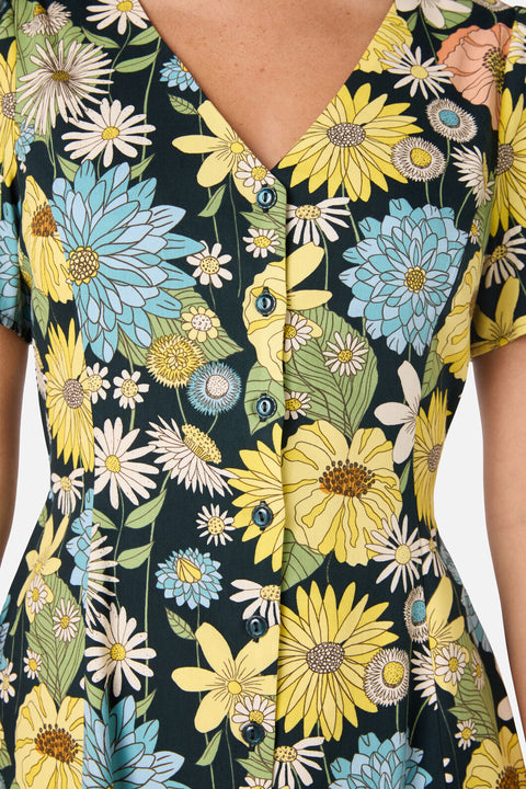 Close-up of a floral dress with yellow, blue, and white flowers on a dark background.