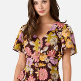 Woman wearing a short sleeve floral blouse with a plain background