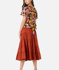 Woman wearing a floral top and tiered rust-colored skirt on a white background