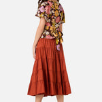 Woman wearing a floral top and tiered rust-colored skirt on a white background