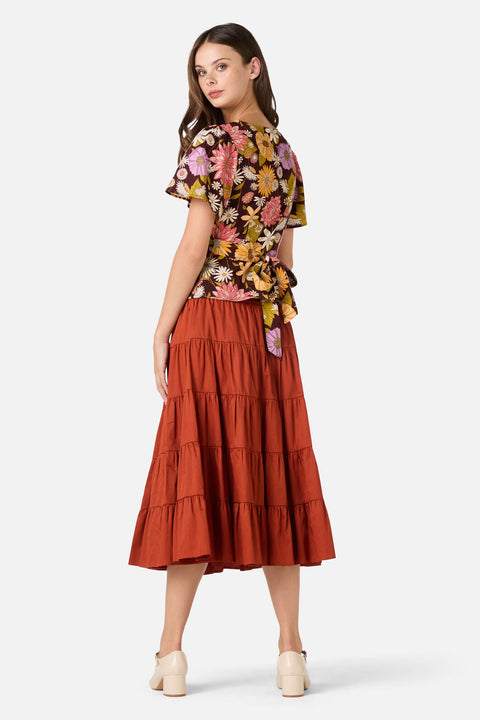 Woman wearing a floral top and tiered rust-colored skirt on a white background