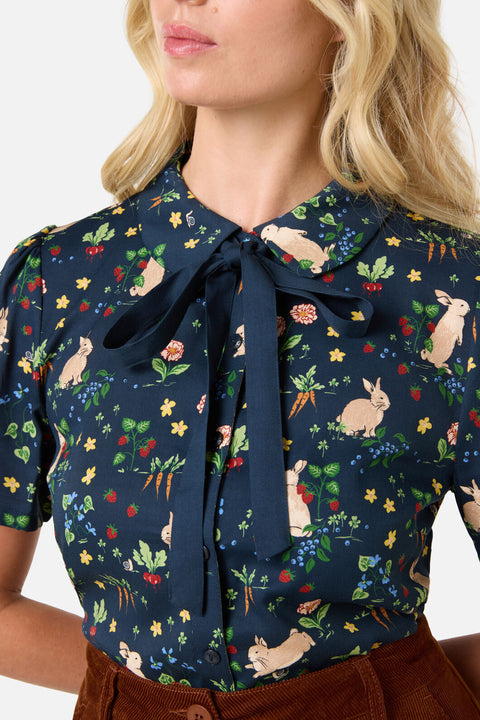 Woman wearing a navy blue blouse with bow, rabbits and colorful floral pattern