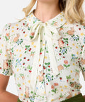 Woman wearing a floral blouse with a tie collar on a white background