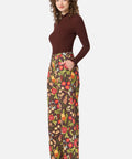 Woman wearing a brown long-sleeve top and floral pants on a white background