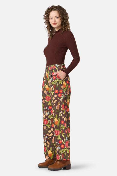 Woman wearing a brown long-sleeve top and floral pants on a white background