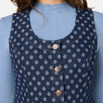 Woman wearing a blue polka dot dress over a light blue sweater against a white background