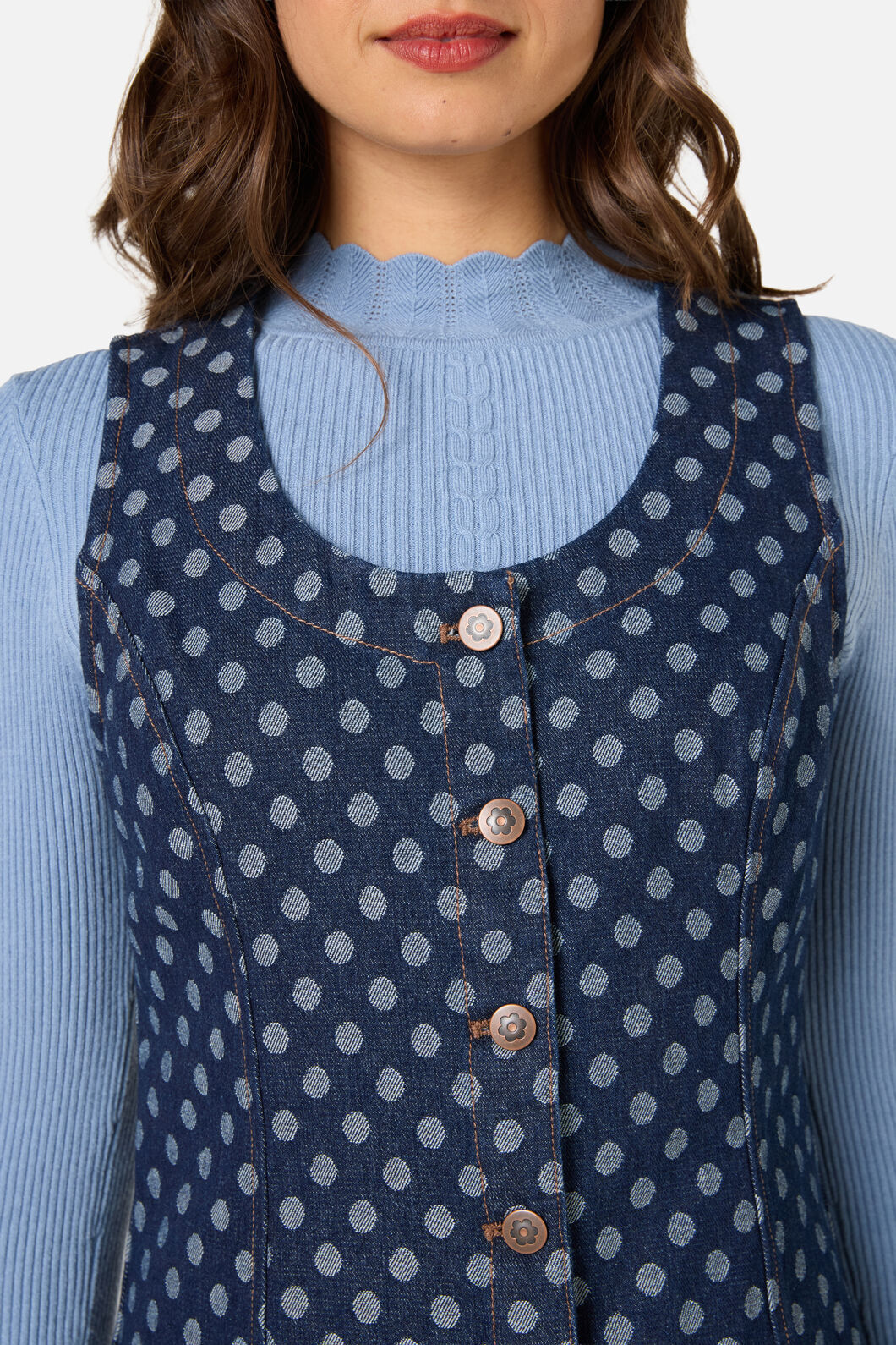 Woman wearing a blue polka dot dress over a light blue sweater against a white background