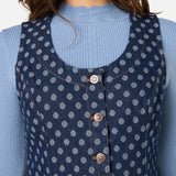 Woman wearing a blue polka dot dress over a light blue sweater against a white background