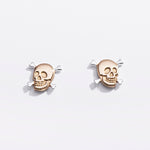 Pair of gold skull earrings on a light gray background