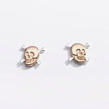 Pair of gold skull earrings on a light gray background