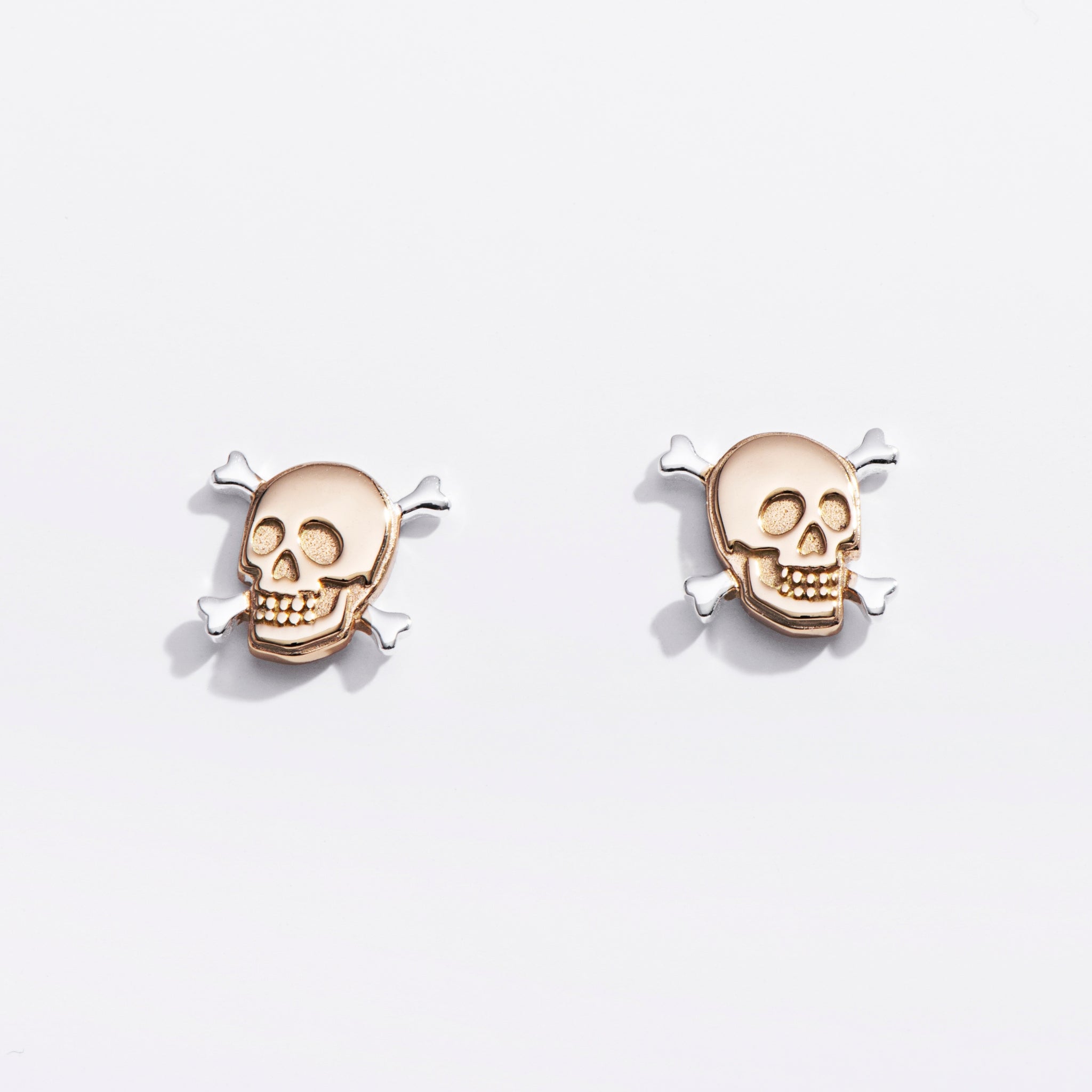 Pair of gold skull earrings on a light gray background