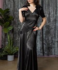 Woman wearing a black satin dress standing against a textured curtain backdrop.