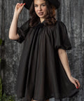 Woman wearing a black dress and hat against a textured gray background