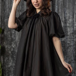 Woman wearing a black dress and hat against a textured gray background