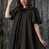 Woman wearing a black dress and hat against a textured gray background