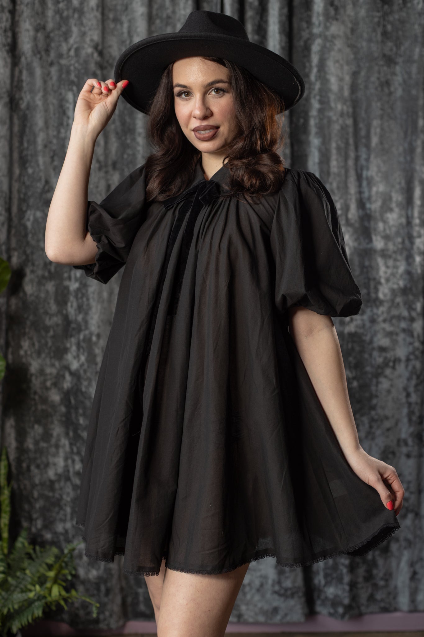 Woman wearing a black dress and hat against a textured gray background