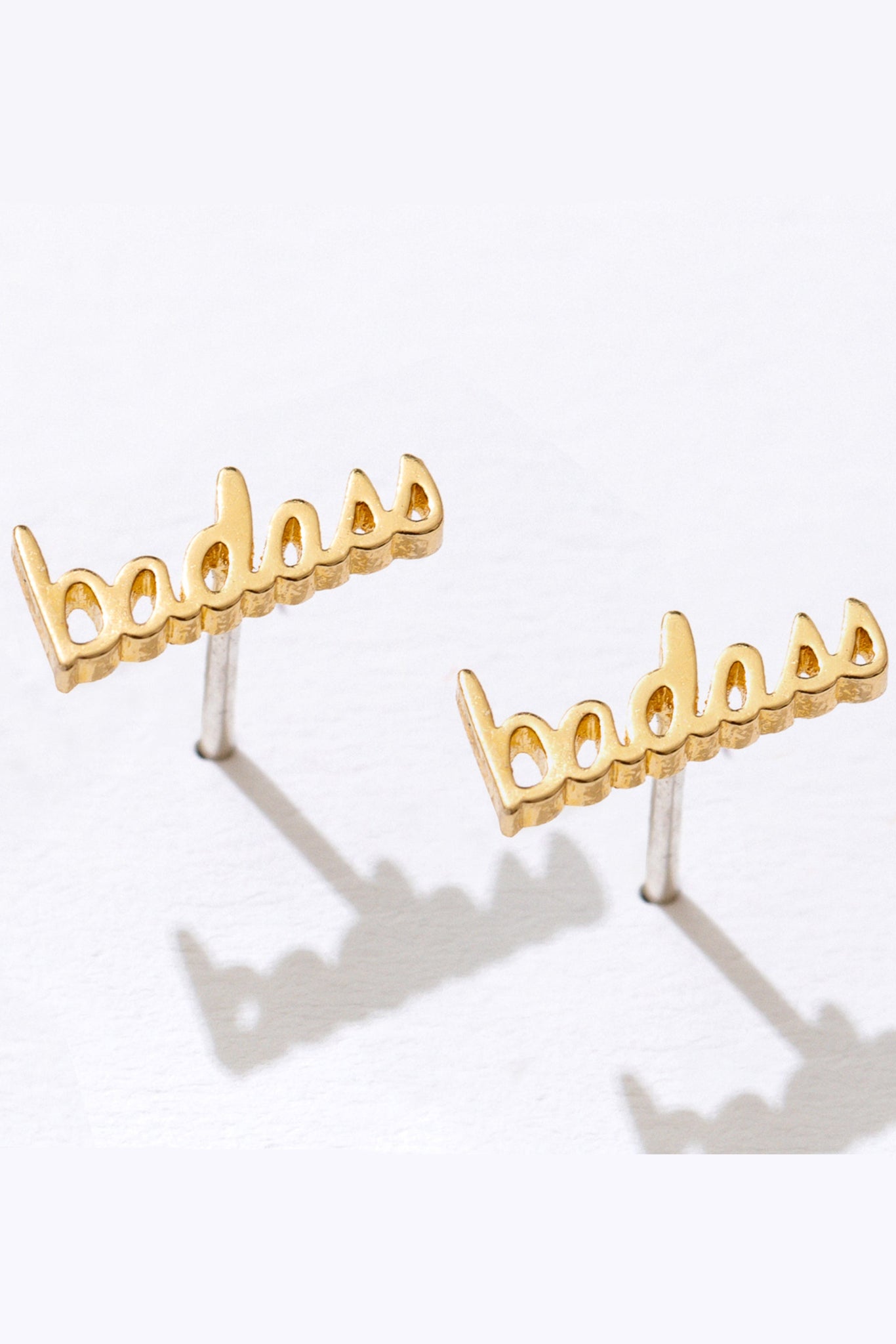 Gold 'badass' earrings on a white background