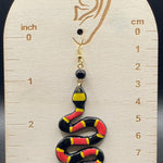 Snake-shaped earring on a wooden display with measurements against a dark background