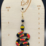 Snake-shaped earring on a wooden display with measurements against a dark background