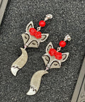 Silver fox-shaped earrings with red accents on a textured surface