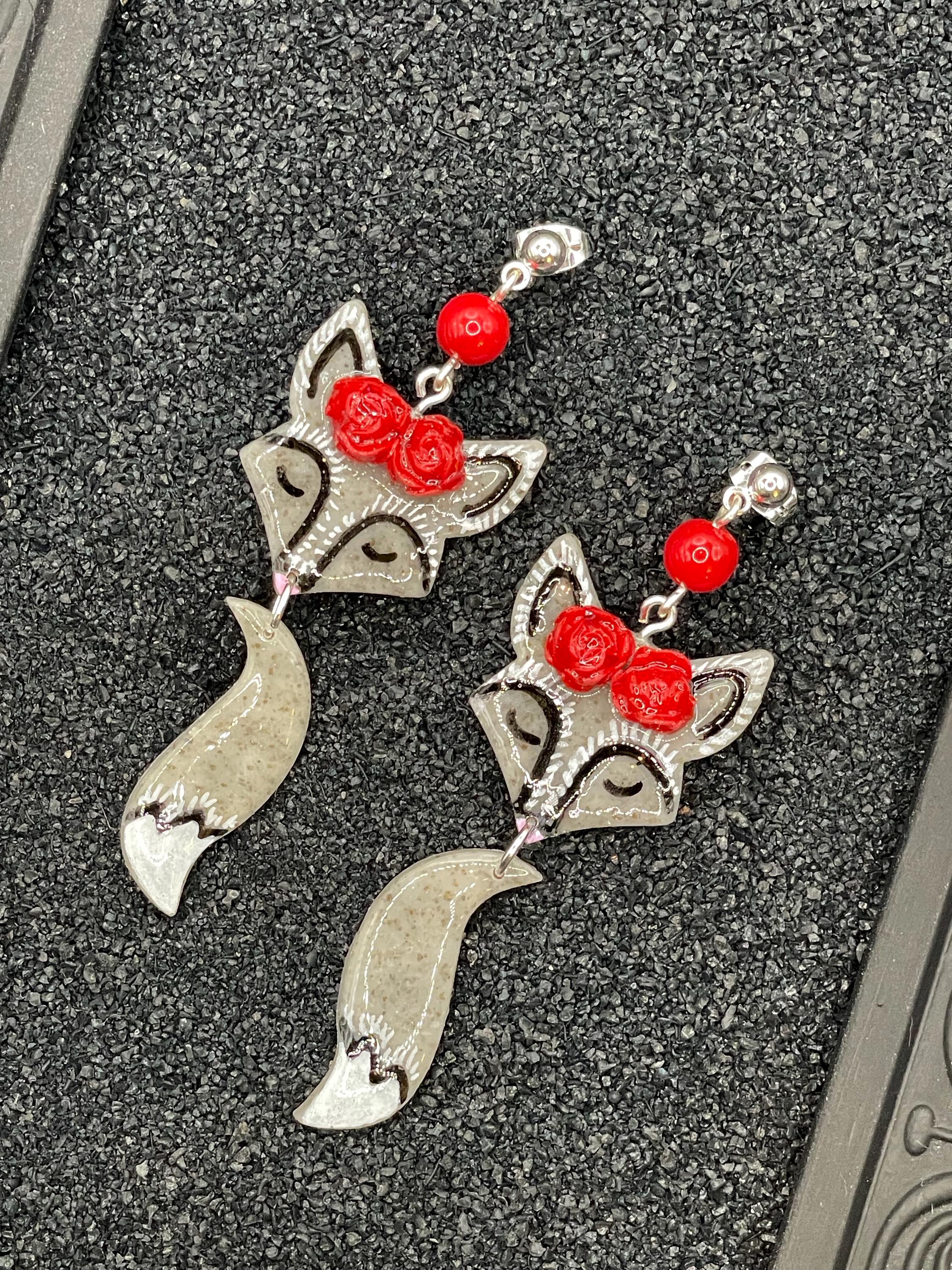 Silver fox-shaped earrings with red accents on a textured surface