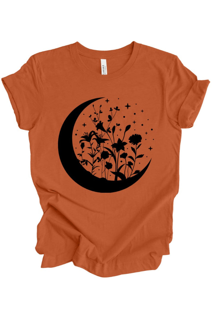 An orange short-sleeve t-shirt with a black graphic of a crescent moon, wildflowers, and stars on the front, displayed on a clean white background.