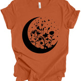 An orange short-sleeve t-shirt with a black graphic of a crescent moon, wildflowers, and stars on the front, displayed on a clean white background.