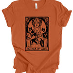 An orange short-sleeve t-shirt with a black graphic print of a woman holding three cats, styled like an Art Nouveau card titled 'MOTHER OF CATS'.