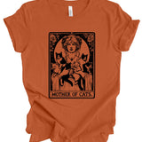 An orange short-sleeve t-shirt with a black graphic print of a woman holding three cats, styled like an Art Nouveau card titled 'MOTHER OF CATS'.