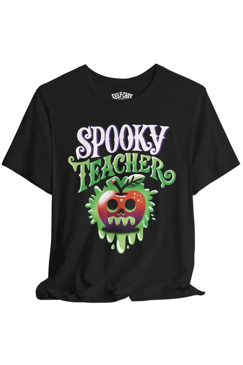 A black short-sleeve t-shirt with a 'Spooky Teacher' graphic on the front, featuring a dripping green slime apple with a skull face. The brand name 'SELF CARE' is printed inside the collar.